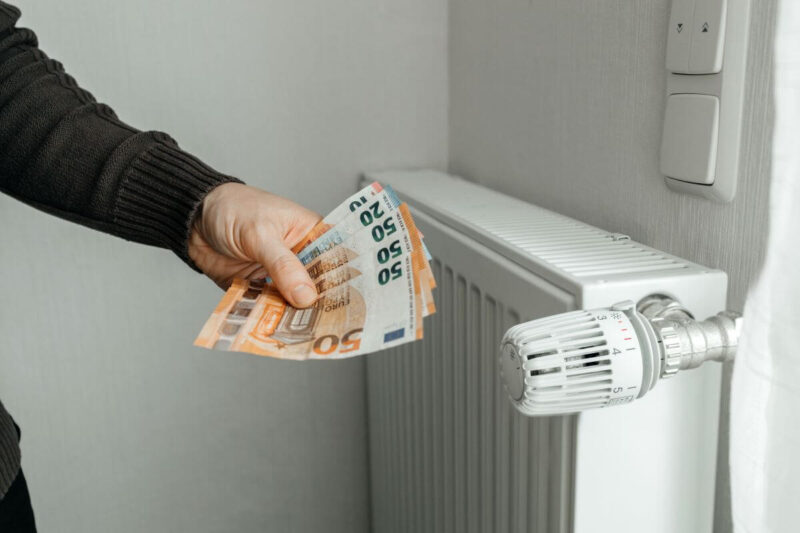 Osoba trzyma banknoty euro przy kaloryferze, symbolizując nadpłaty za centralne ogrzewanie.