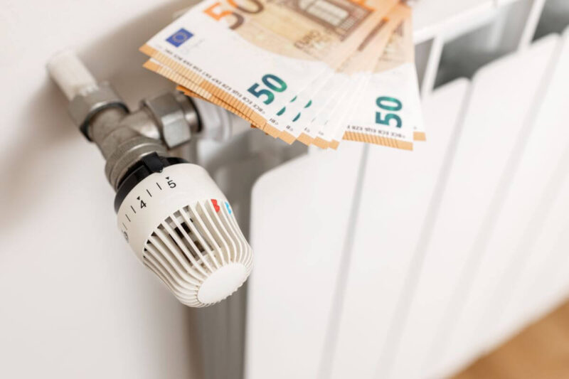 Termostat na kaloryferze z banknotami euro, symbolizujący rozliczanie kosztów centralnego ogrzewania w spółdzielniach.