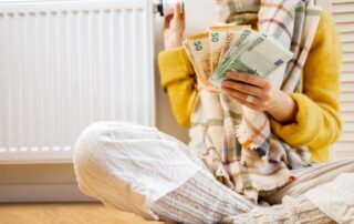 Osoba przy grzejniku trzyma gotówkę, sugerując dopłatę za ogrzewanie.
